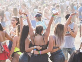 3 filles au milieu de la foule, avec les mains en l'air, qui portent des bracelets en tissu lors d'un festival en plein air